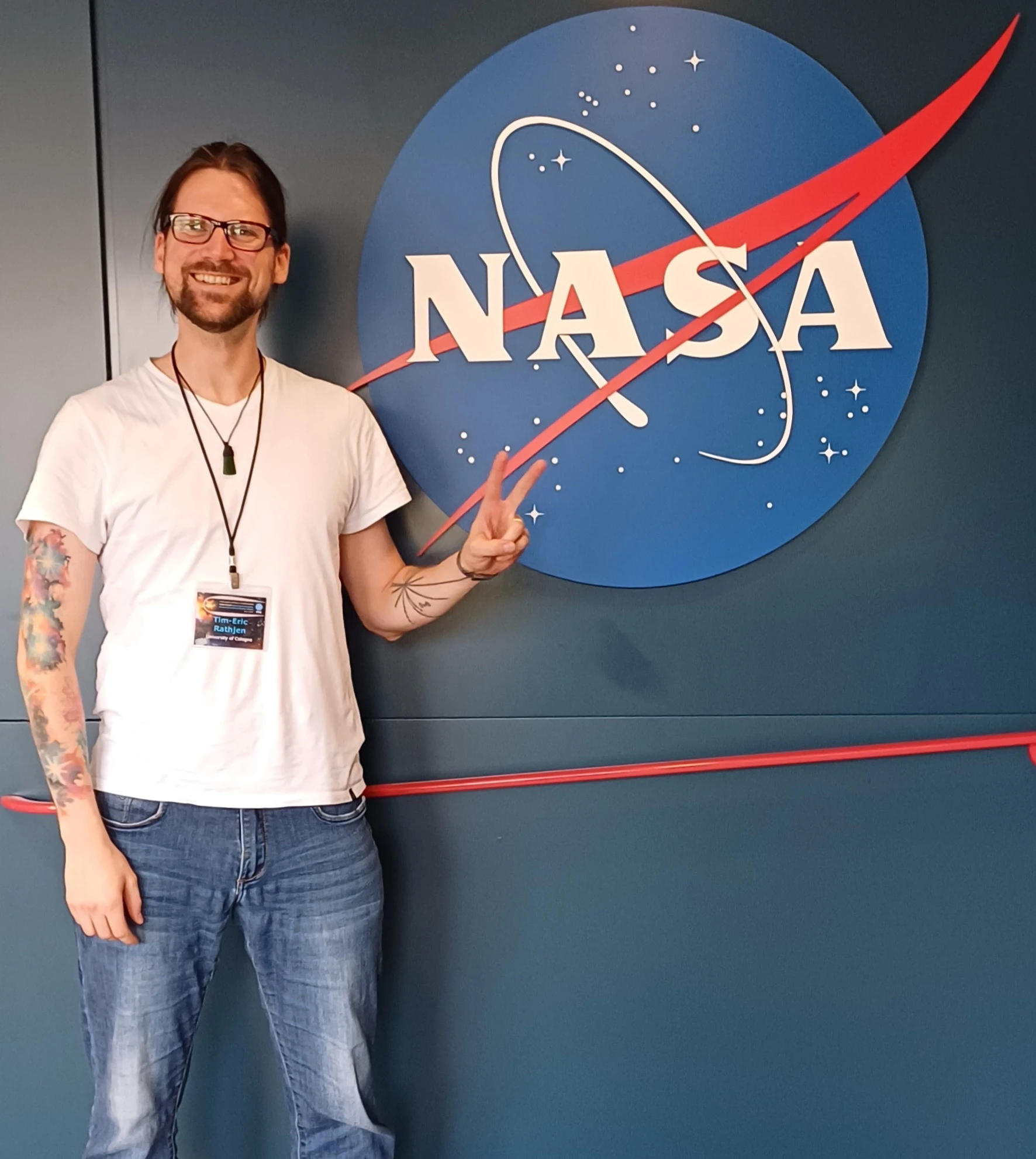 A smiling visitor pointing to a large NASA emblem on a wall.